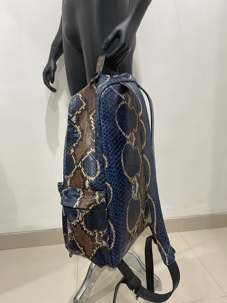 Op de afbeelding: Een blauwe en bruine slangleren rugzak met verstelbare banden. De rugzak heeft een ritsvak aan de voorkant.