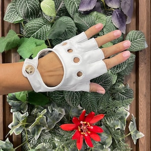 May include: White leather driving gloves with fingerless design and a gold button closure. The gloves have multiple perforations for breathability.