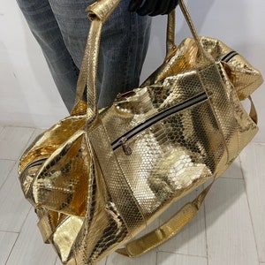 May include: A gold-coloured snakeskin duffel bag with a zipped pocket and a shoulder strap.