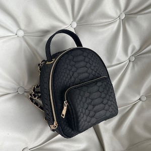 May include: A black snakeskin backpack with gold hardware and a chain strap.