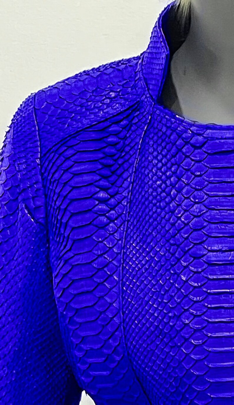 K&ouml;nnte beinhalten: Eine leuchtend blaue Schlangenlederjacke mit Rei&szlig;verschluss. Die Jacke hat ein strukturiertes, schuppiges Muster.