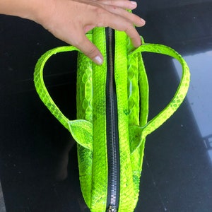 May include: A bright neon green handbag with a zipper closure and two top handles. The bag is made of snakeskin.
