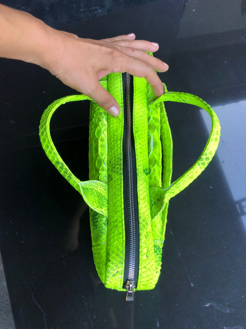 May include: A bright neon green handbag with a zipper closure and two top handles. The bag is made of snakeskin.