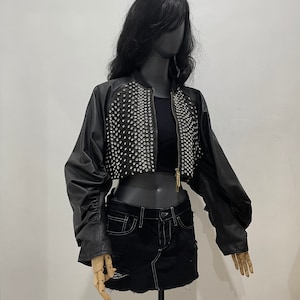 May include: A black cropped bomber jacket with a zipper closure and a studded design on the front. The jacket has long sleeves and a relaxed fit.