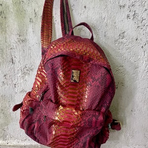 May include: A red and gold snakeskin backpack with a zip closure and adjustable straps.