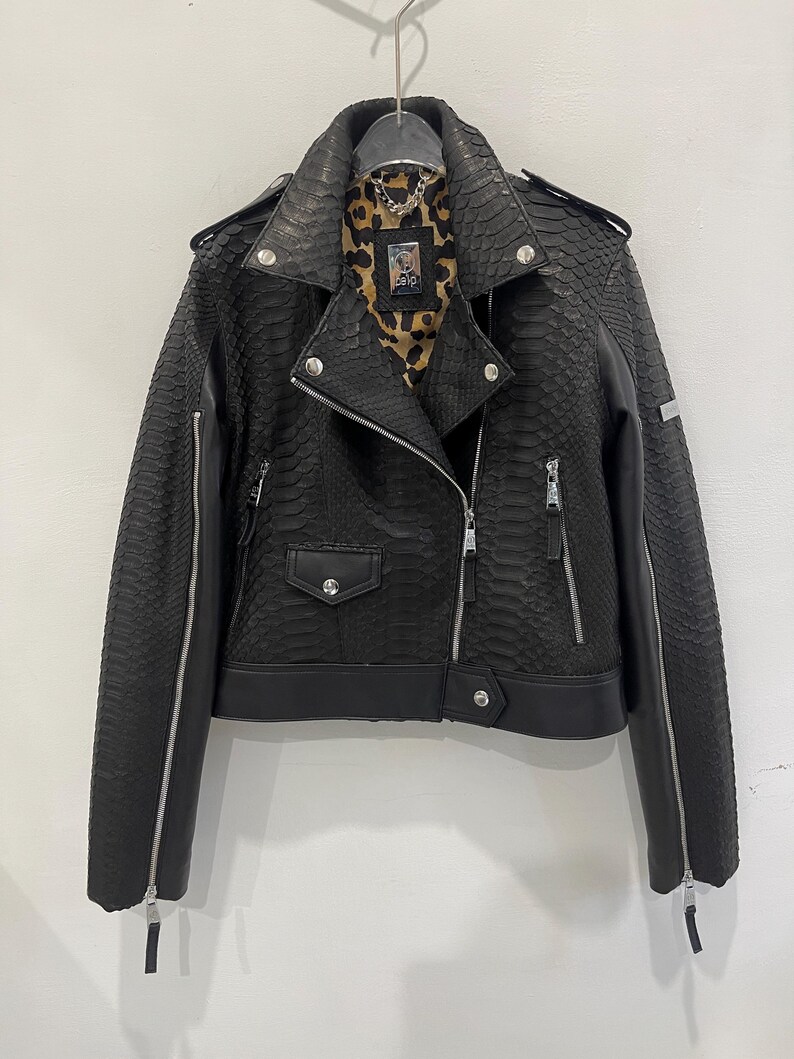 Może przedstawiać: Czarna sk&oacute;rzana kurtka motocyklowa ze wzorem sk&oacute;ry węża i zamkiem błyskawicznym. Kurtka ma podszewkę w panterkę i srebrny suwak.