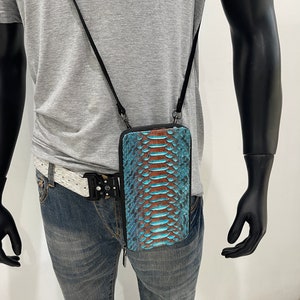 May include: A blue and brown snakeskin leather phone case with a black strap. The case is worn on a person's hip.