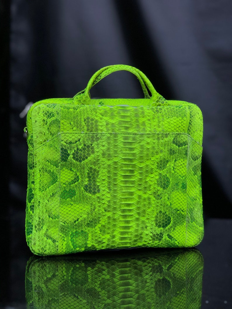 May include: A bright green snakeskin laptop bag with a top handle. The bag has a textured surface and a flap closure.