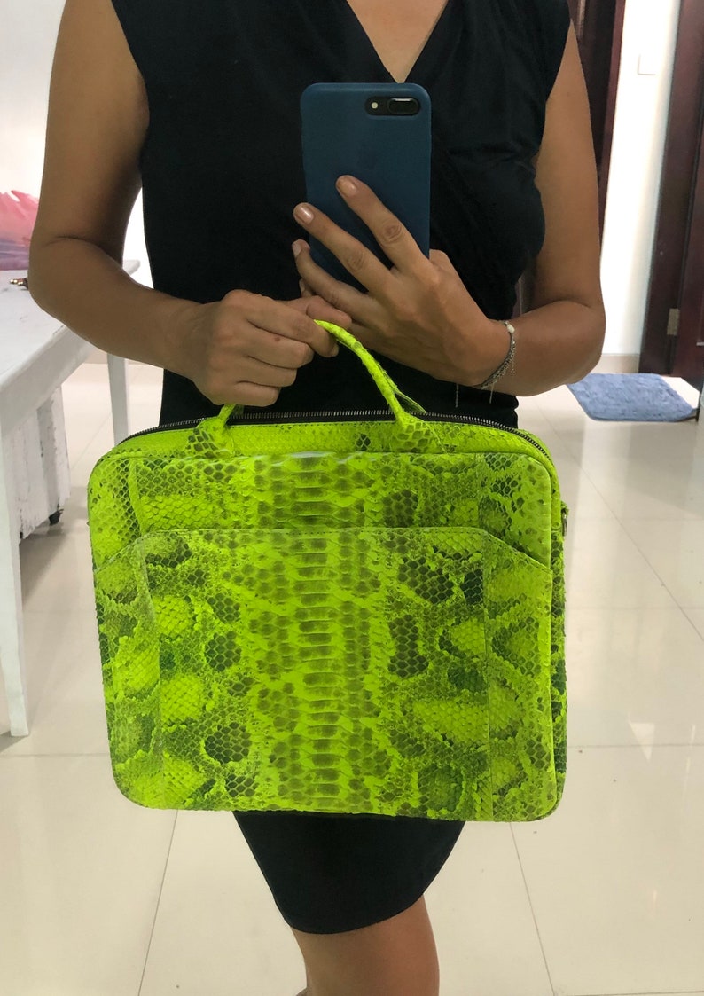 May include: A bright green snakeskin laptop bag with a zipper closure. The bag has a top handle and a shoulder strap.