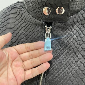 May include: Black leather jacket with a zip fastening and a snakeskin pattern. The jacket has two silver buttons on the collar.