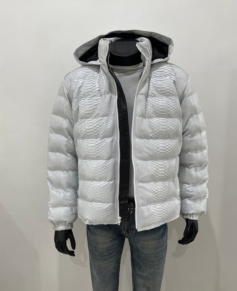 May include: White puffer jacket with a snakeskin pattern. The jacket has a hood and a zip closure.