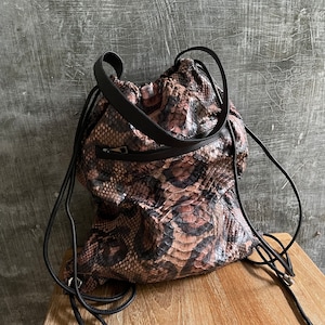 May include: A pink and black snakeskin drawstring backpack with black straps and silver hardware.