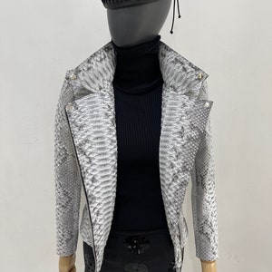 以下が含まれることがあります： ジッパー留めの白いヘビ柄の革ジャン。スタンドカラーと長袖です。