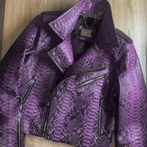 May include: A purple snakeskin leather jacket with a zipper closure and a silver chain detail on the collar. The label "Gabor" is visible on the inside of the collar.