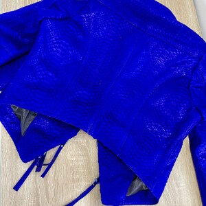 K&ouml;nnte beinhalten: Eine blaue Schlangenlederjacke im Cropped-Stil mit Rei&szlig;verschl&uuml;ssen. Die Jacke hat eine strukturierte Oberfl&auml;che und ein einzigartiges Design.