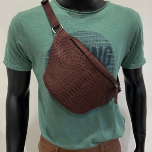 May include: A brown leather fanny pack with a snakeskin pattern. The bag has a zipper closure and a strap that goes over the shoulder.