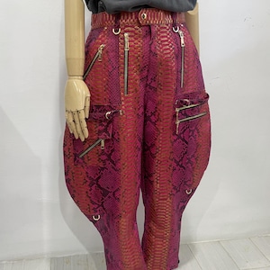 May include: Pink and orange snakeskin pants with gold zippers and hardware. The pants have a wide leg and a relaxed fit.
