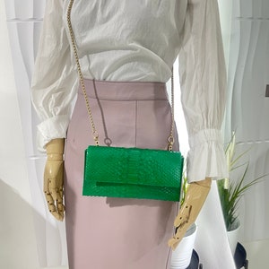 May include: A green snakeskin clutch bag with a gold chain strap. The bag is closed and has a flap with a gold clasp.