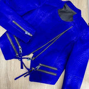 K&ouml;nnte beinhalten: Eine leuchtend blaue Schlangenlederjacke mit mehreren Rei&szlig;verschl&uuml;ssen. Die Jacke hat einen Stehkragen und lange &Auml;rmel.