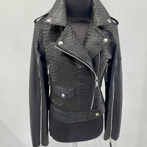 Może przedstawiać: Czarna sk&oacute;rzana kurtka ze wzorem sk&oacute;ry węża. Kurtka ma zamek błyskawiczny, dwie kieszenie i srebrny suwak.