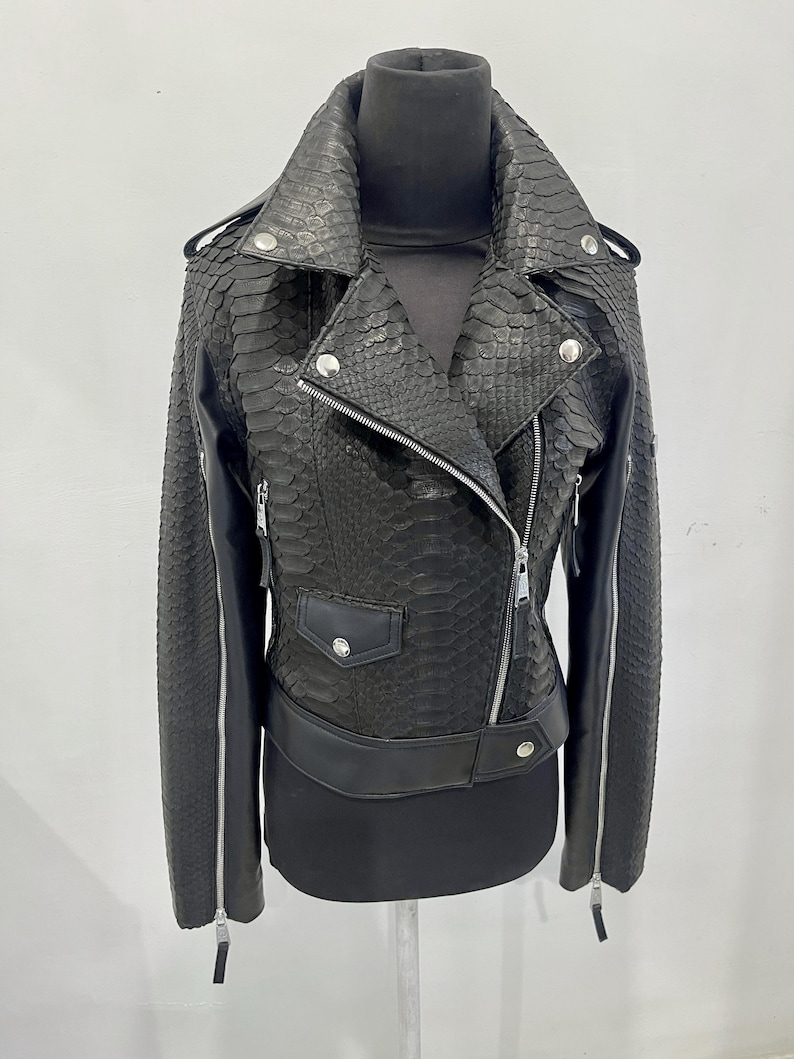 Może przedstawiać: Czarna sk&oacute;rzana kurtka ze wzorem sk&oacute;ry węża. Kurtka ma zamek błyskawiczny, dwie kieszenie i srebrny suwak.