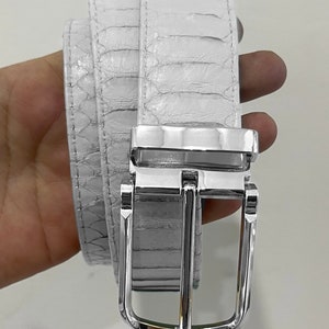 May include: White belt with a textured, reptile-like pattern. The belt has a silver-coloured, rectangular buckle with a single prong. The belt is made of a flexible material and appears to be new.