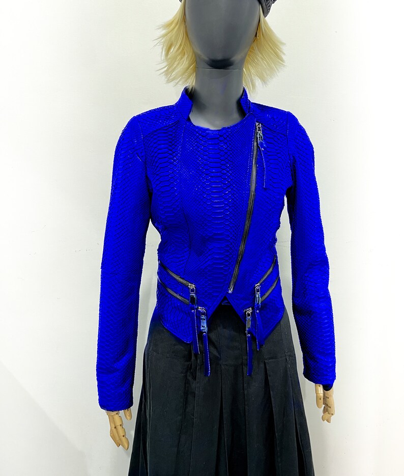 K&ouml;nnte beinhalten: Eine blaue Lederjacke mit Schlangenhautmuster und Rei&szlig;verschlussdetails. Die Jacke hat eine verk&uuml;rzte L&auml;nge und einen Stehkragen.