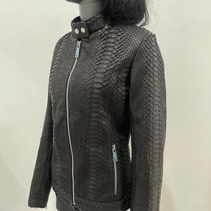 May include: Black leather jacket with a snakeskin pattern. The jacket has a zip closure and two zipped pockets.