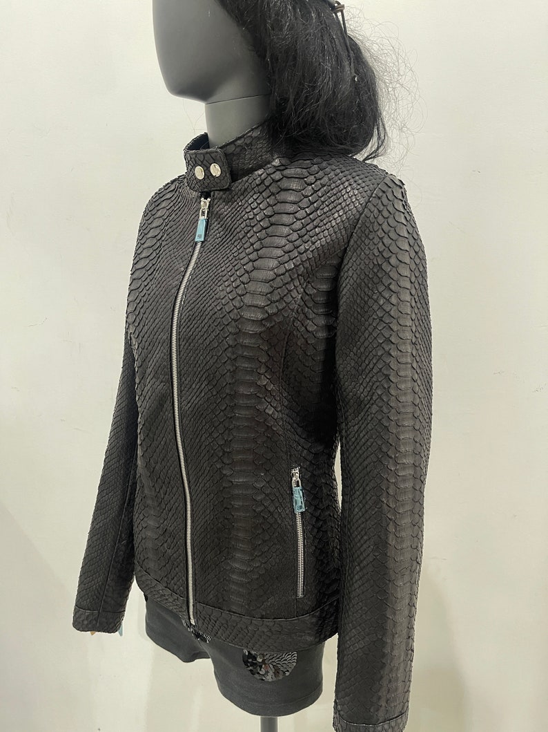 May include: Black leather jacket with a snakeskin pattern. The jacket has a zip closure and two zipped pockets.