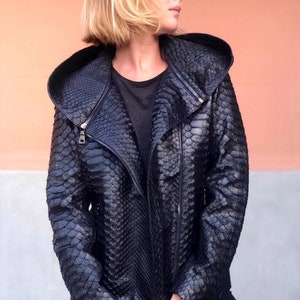 May include: A black leather jacket with a hood, made from snakeskin. The jacket has a zipper closure and an asymmetrical design.
