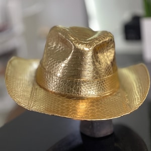 May include: A gold cowboy hat with a textured, snakeskin-like pattern.