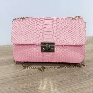 May include: A pink snakeskin shoulder bag with a gold chain strap and a gold lock closure.