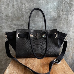 May include: Black leather handbag with a snakeskin pattern and a silver buckle closure. The bag has a top handle and a long adjustable shoulder strap.