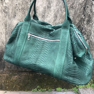 May include: A green leather duffel bag with a snakeskin pattern. The bag has a zipper closure and two top handles.