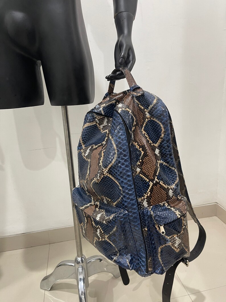 Op de afbeelding: Een blauwe en bruine slangleren rugzak met een ritsvak aan de voorkant. De rugzak heeft een bovenste handvat en verstelbare banden.