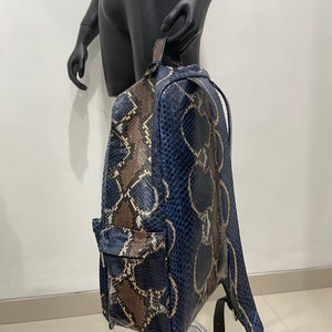 Op de afbeelding: Een blauwe en bruine slangleren rugzak met verstelbare banden. De rugzak heeft een ritsvak aan de voorkant.