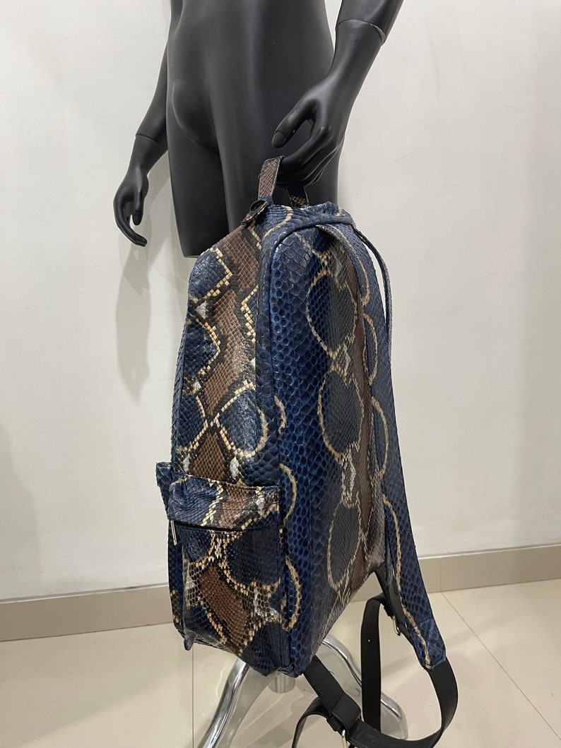 Op de afbeelding: Een blauwe en bruine slangleren rugzak met verstelbare banden. De rugzak heeft een ritsvak aan de voorkant.