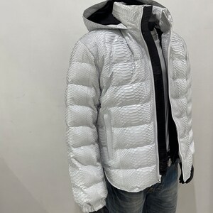 May include: A white puffer jacket with a snakeskin pattern. The jacket has a hood and a zip closure.