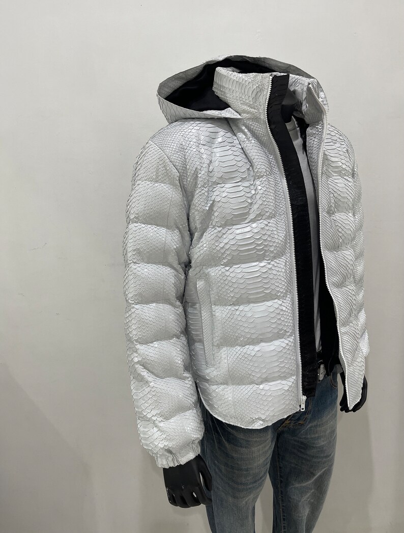May include: A white puffer jacket with a snakeskin pattern. The jacket has a hood and a zip closure.