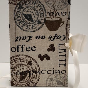 May include: A beige fabric box with a white ribbon. The box has a coffee theme with brown coffee beans, a cup of coffee, and the words "Coffee", "Latte", and "Cappuccino" printed on it.