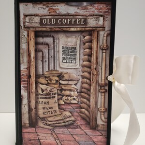 May include: A vintage-style book with a black frame and a brown and white image of a coffee warehouse. The image features a doorway with a sign that reads "Old Coffee" and a bag of coffee beans labeled "Clean Coffee". The book is tied with a white ribbon.