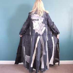 May include: A floor-length patchwork denim coat in black, grey, and white. The coat is made from various denim patches and pockets, with white fabric accents. The design is artistic and unique, showcasing a variety of textures and patterns.