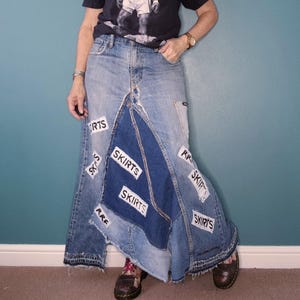 May include: A patchwork denim skirt in various shades of blue. The skirt is adorned with patches and the word "SKIRTS" in white. It has a frayed hem, creating a distinctive and eye-catching style. The skirt's design is unique.