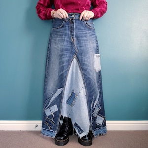 May include: A long denim skirt made from multiple pieces of denim sewn together. The skirt has a patchwork design with different shades of blue denim. The skirt is maxi length and has a slit in the front.