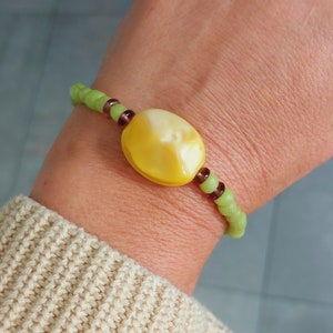 Könnte beinhalten: Ein grünes und braunes Perlenarmband mit einer großen gelben Bernsteinperle.