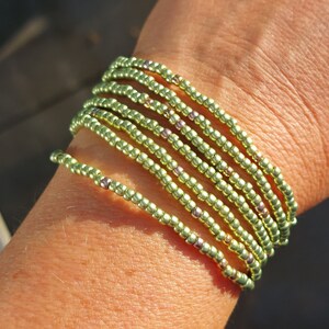 Op de afbeelding: Een armband gemaakt van meerdere strengen lichtgroene kralen. De kralen zijn klein en rond en zijn aan elkaar geregen om een gelaagd effect te creëren.