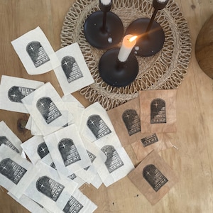 May include: A collection of fabric squares featuring a black and white print of a building with a star on top. The fabric squares are arranged on a wooden surface. There are three black candle holders with white candles on a woven placemat.