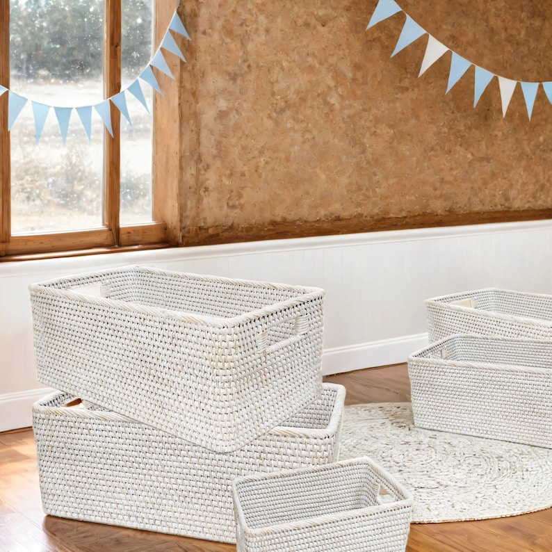 May include: Four white wicker storage baskets with handles. The baskets are stacked on top of each other and are sitting on a wooden floor.