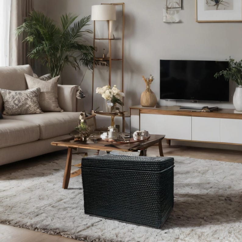 May include: Black woven storage ottoman with a textured surface. The ottoman is in a living room setting with a couch, coffee table, and a television.