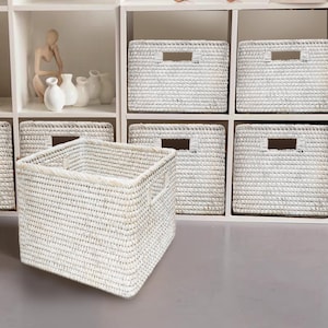 May include: White wicker storage baskets with handles, arranged on a white shelf unit. The baskets are woven with a fine, intricate pattern.